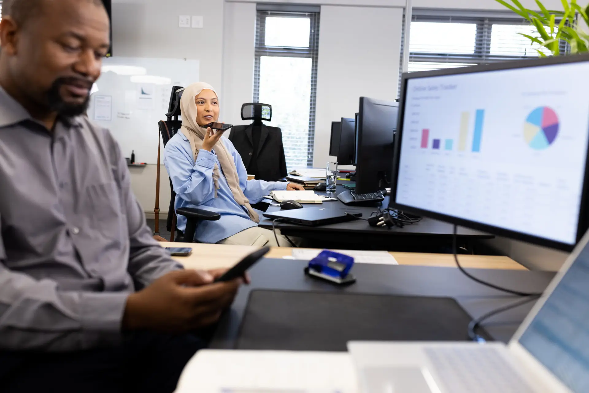 Happy african american businessman with smartphone sitting at desk in office. Business professionals, job, corporation and working in office concept.